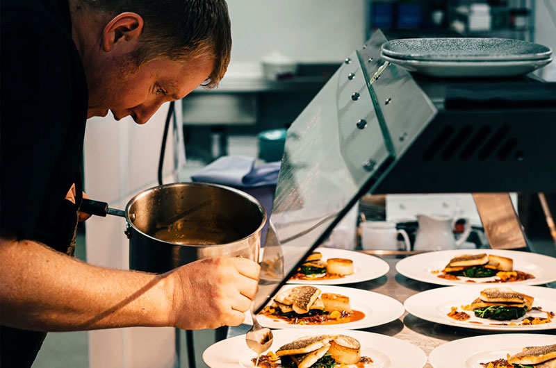 chef putting sauce on plates of food in a restaurant kitchen